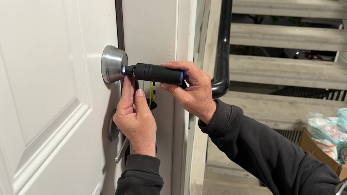 Close-up of locksmith hands using a specialized decode tool on a Kwikset SmartKey deadbolt