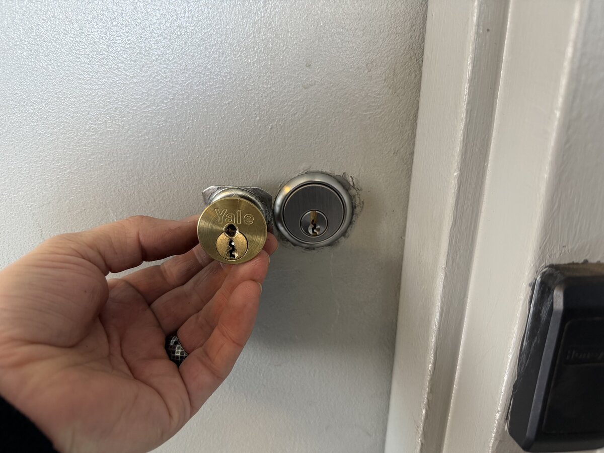 Hand holding old Yale lock cylinder next to newly installed deadbolt — the cylinder had come loose and the tailpiece was no longer engaging