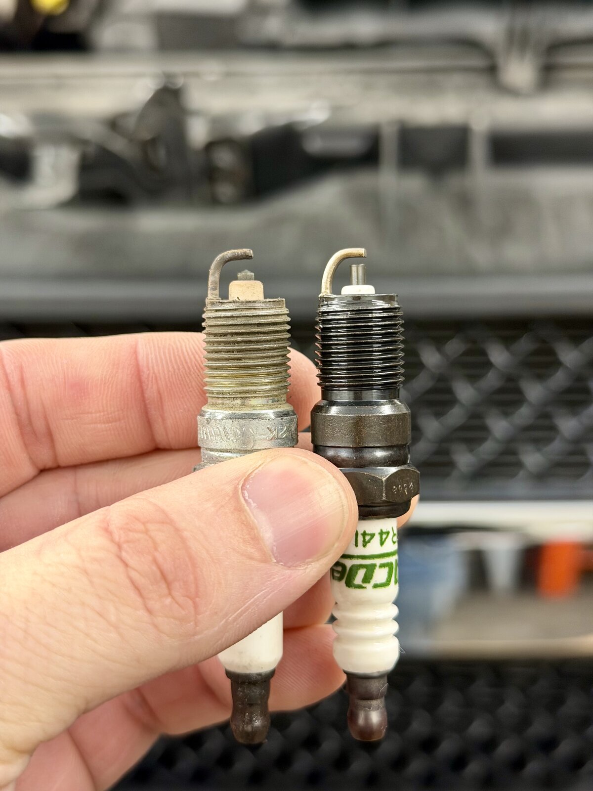 Old worn spark plug next to brand new ACDelco replacement spark plug